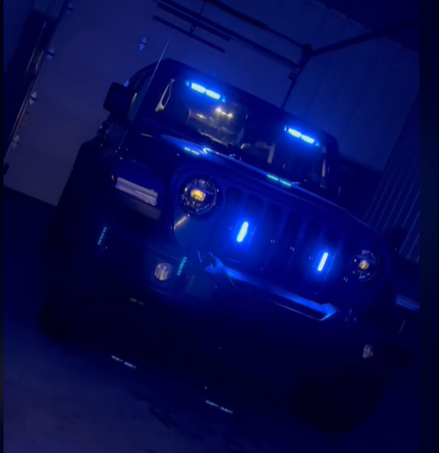 Jeep Wrangler with blue LED warning lights illuminated across the grille, hood, and windshield in a garage