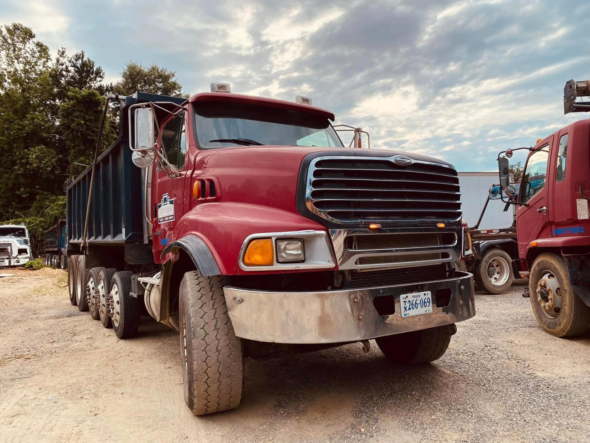 Red Sterling dump truck in a commercial fleet yard with chrome bumper and grille